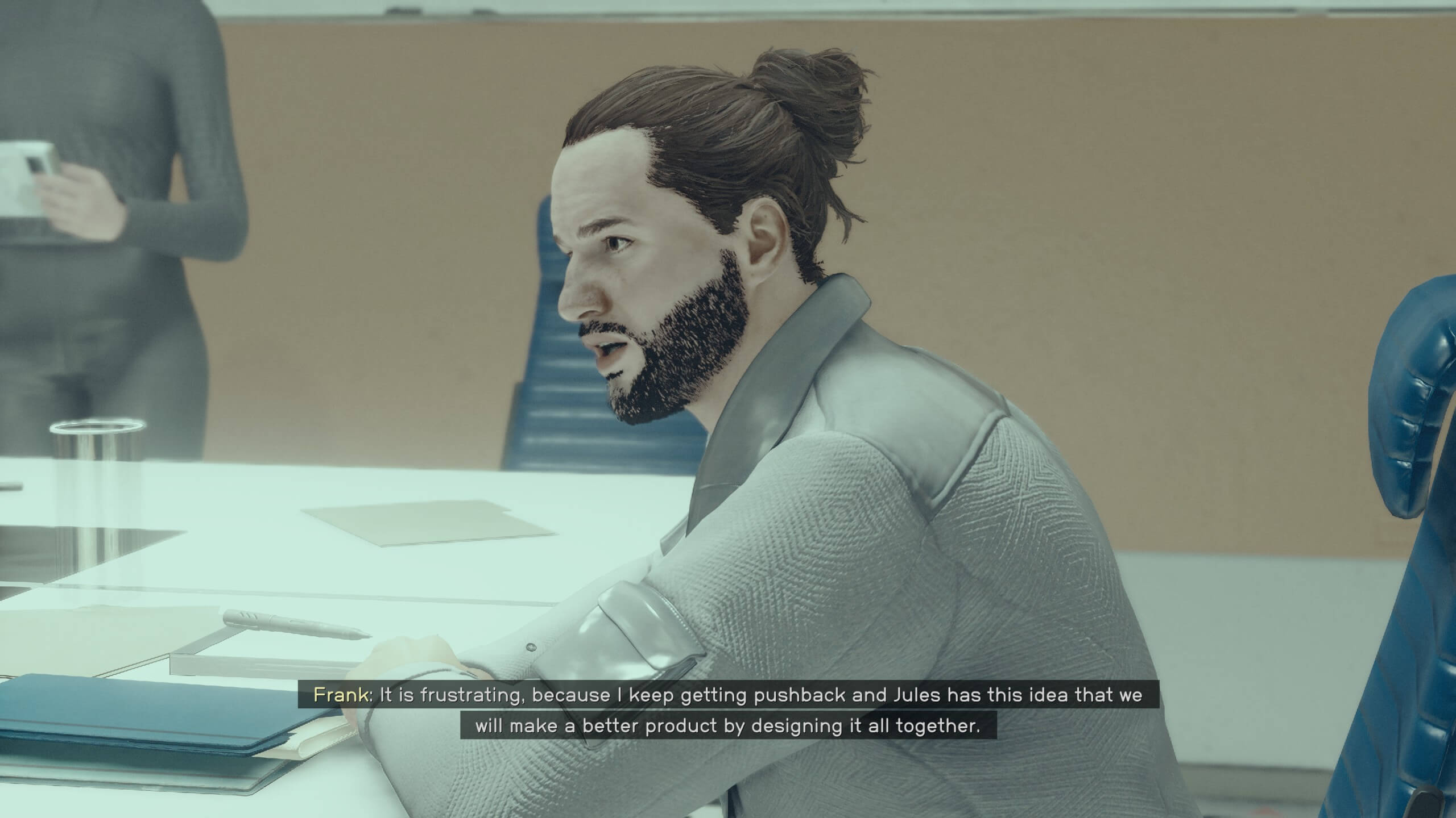 The player is talking to a designer named Frank. He is sitting at a table saying "It is frustrating because I keep getting pushback and Jules has this idea that we will make a better product by designing it all together."